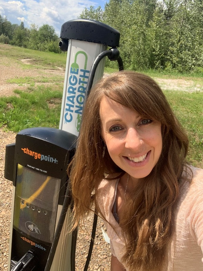 Smiling woman in front of electric vehicle charging station.